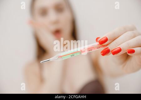 Junge Frau im Alter krank mit Windpocken, hält Thermometer und misst Temperatur Stockfoto