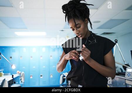 Afroamerikanische Spezialistin mit Dreadlocks einstellen und einschalten Lampe aus binokularen Gläsern während der Arbeit im zeitgenössischen Labor Stockfoto