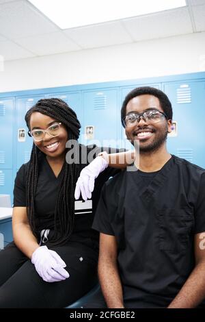 Glückliche afroamerikanische Frau mit Zöpfen und schwarzem bärtigen Mann, der lächelt und die Kamera anschaut, während sie im modernen Labor Prothesen kreiert Stockfoto