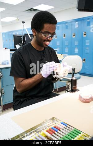 African American Kerl in Latexhandschuhe mit Mund Spiegel und Sonde zur Überprüfung falscher Zähne bei der Arbeit im modernen Labor Stockfoto