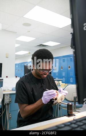 African American Kerl in Latexhandschuhe mit Mund Spiegel und Sonde zur Überprüfung falscher Zähne bei der Arbeit im modernen Labor Stockfoto