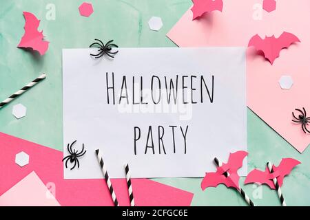 Text Halloween Party auf geschichteten Papier Hintergrund in mintgrün und pastellrosa. Flaches Lay, Halloween Party Dekor - Hexagon Konfetti, Papier Trinkstr Stockfoto