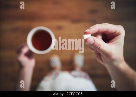 Kranker junger Mann in Nachtwäsche nimmt Pillen und trinkt heißen Tee. Themen Gesundheit, Genesung und Prävention von Krankheiten. Stockfoto