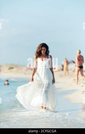Frau in hellweißem Kleid am Strand spazieren und suchen Nach unten Stockfoto