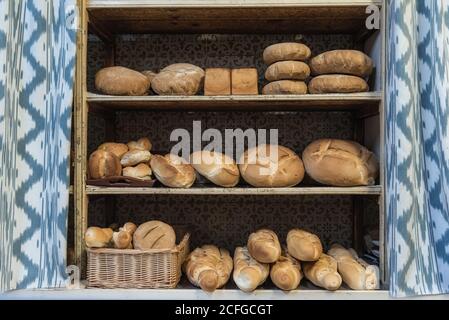 Laibe mit verschiedenen frischen Brot zum Verkauf auf Shabby platziert Regale in der Nähe von Vorhängen in der Bäckerei Stockfoto