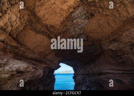 Rauer Bogengang aus Steinhöhle, der an sonnigen Tagen auf Ibiza, Spanien, zum ruhigen blauen Meer in Cala Conta führt Stockfoto