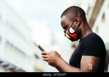Nahaufnahme Porträt eines afroamerikanischen Mannes mit einer bunten Maske. Er benutzt ein Handy mit ernsthafteren Ausdrücken Stockfoto