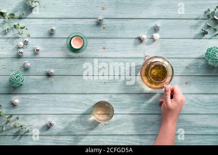 Wintertee, Arrangement mit Glas-Teekanne, Glas Tee in der Hand auf hellblauem minzholzigen Hintergrund. Weihnachtsschmuck, Disco Bälle, Kugeln, Stockfoto