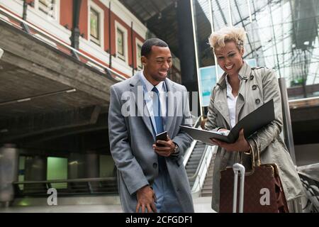 Fröhlich lachende schwarze Männer und Frauen in trendigen eleganten Kleidern, die Spaß haben, während sie mit Papieren auf Treppen stehen. Stockfoto
