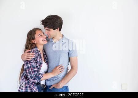 Junges Paar in Freizeitkleidung Umarmung im Zimmer mit weiß Leere Wand Stockfoto