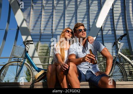 Hübscher junger Mann und hübsche Frau saßen an sonnigen Tagen in der Nähe von Fahrradfahrern Stockfoto