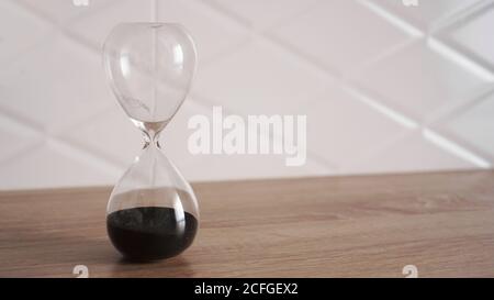 Kristall Sanduhr mit schwarzem Sand auf Holztisch und weiß Hintergrund Stockfoto