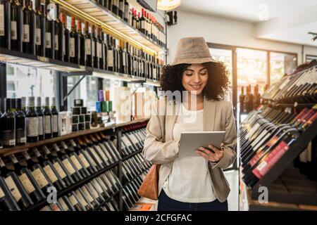 Trendige lockige Frau hält Tablet auf dem Weinmarkt. Stockfoto