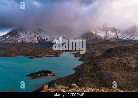 Von oben atemberaubende Landschaft von ruhigen Fluss mit türkisfarbenem Wasser Im Hochland gegen verschneite Berge Gipfeln inmitten dramatischer Wolken Stockfoto