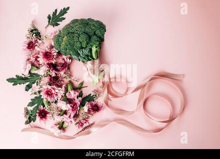 Draufsicht auf Strauß hübscher Blumen und reifer Brokkoli Mit Seidenband auf rosa Hintergrund am Sommertag angeordnet Stockfoto