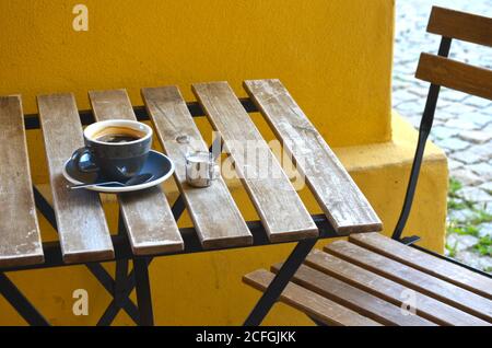 Espresso Lungo Kaffee in einer blauen Tasse mit Milch in Ein kleiner Metallkrug auf einem Holztisch auf einem Gelber Wandhintergrund Stockfoto