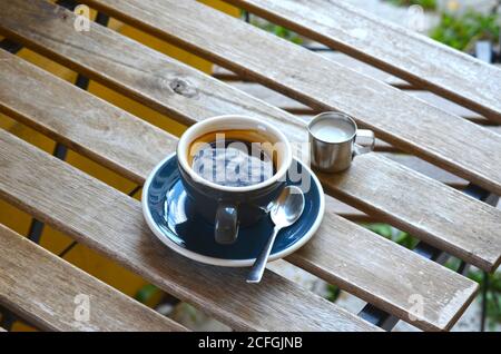 Espresso Lungo Kaffee in einer blauen Tasse mit Milch in Ein kleiner Metallkrug auf einem Holztisch Stockfoto