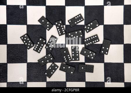 Zufällig verstreute schwarze Domino-Fliesen auf einem schwarz-weiß Schachbrett von oben betrachtet in einem Konzept der persönlichen Unterhaltung Stockfoto
