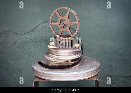 Alte gestapelte Vintage-Film-Filme mit verschiedenen Durchmessern mit einem Projektorrolle aufrecht auf einem strukturierten Grün stehend Hintergrund mit Vignette in Stockfoto