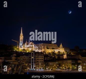 Mond steigt über Buda auf: Im Blick von Pest steigt der Mond über die Fischerbastei, die Matthias-Kirche und das Hilton Hotel im Burgviertel von Buda auf. Stockfoto