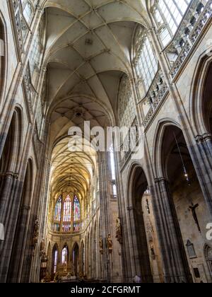 Veitsdom Innenraum: Die hohen Säulen und die hohe Decke umrahmen die Altarfenster und die Vorderseite der Prager Kathedrale. Eine Frau betet. Stockfoto