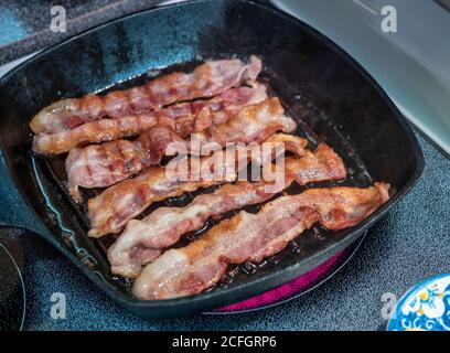 Sechs Scheiben knusprigen Speck Braten: Sechs Rascher Speck Blase in einer schweren gusseisernen Pfanne auf einem elektrischen Herd oben erhitzt. Stockfoto