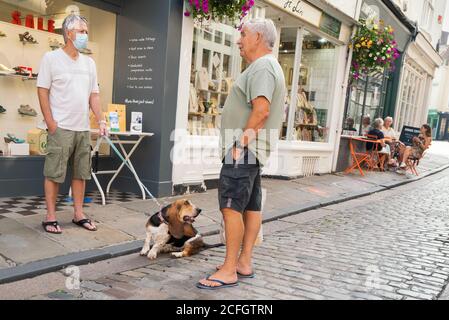 Canterbury, UK - 13. August 2020 ein Mann, der wegen Covid 19 eine Maske trägt und einen Basset Hund an der Leine hält, hat ein Gespräch, das auf einem Quai steht Stockfoto