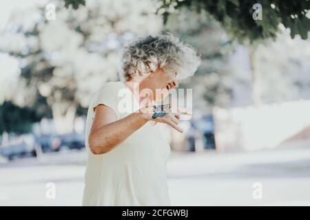 Cool edgy kaukasischen alte Dame Frau mit Schmetterling Tattoo auf der Hand. Schöne funky ältere Frau mit weiß grauen Haaren machen Teufel Rock Zeichen Stockfoto