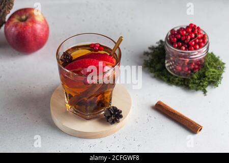 Trendfoto von heißem Tee im Herbst oder Winter mit Zimt, Zitrone, Apfel, Beeren und Gewürzen in einer transparenten Tasse. Stockfoto