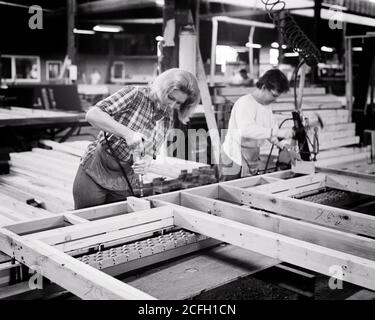 1960S 1970S ZWEI ARBEITERFRAUEN AUF FERTIGFABRIKBODEN MONTAGE EIN HOLZRAHMEN FÜR DEN EINSATZ IN FERTIGBAUTEN - I5633 HAR001 HARS HALF-LENGTH DAMEN PERSONEN BERUF B & W GESCHICKLICHKEIT BERUF FÄHIGKEITEN FRAUENRECHTE BEI GLEICHEM LOHN KARRIERE ZUSAMMENSTELLEN VON INNOVATIONEN ARBEITSBERUFE GLEICHBERECHTIGUNG MITARBEITER FERTIGFERTIGUNG GLEICHHEIT MITTE ERWACHSENE MITTE ERWACHSENE FRAU PRÄZISION VORFERTIGUNG VERWENDEN SIE JUNGE ERWACHSENE FRAU SCHWARZ UND WEISS KAUKASISCHEN ETHNIZITÄT HAR001 DIE ARBEIT IST ALTMODISCH Stockfoto