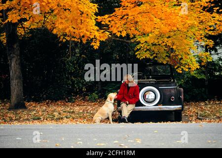 LÄCHELNDE FRAU DER 1990ER JAHRE IN ROTEM MANTEL IM HERBST WALDLANDSCHAFT SITZEN AUF ANTIKEN AUTO STOSSSTANGE STREICHELN GELB LABRADOR RETRIEVER HUND - KD6106 WAL004 HARS LAB NOSTALGISCHE HERBST SCHÖNHEIT VERLÄSST VORSTADT GELB INLÄNDISCHEN FARBE BEZIEHUNG EINSTELLUNG PET CABRIO ALTEN ZEIT NOSTALGIE OLD FASHION AUTO 1 JUGENDLICH STIL FAHRZEUG SICHERHEIT JUNGEN ERWACHSENEN FRIEDEN TEAMARBEIT FREUDE LIFESTYLE FRAUEN LÄNDLICHEN ERWACHSENEN GESUNDHEIT TRANSPORT KOPIEREN RAUM IN VOLLER LÄNGE DAMEN PERSONEN AUTOMOBIL CARING LABRADOR GELASSENHEIT VERTRAUEN TRANSPORT BLICKKONTAKT FARBENFROHE FREIHEIT GLÜCK SÄUGETIERE WELLNESS FRÖHLICHE FREIZEIT STÄRKE AUTOS Stockfoto