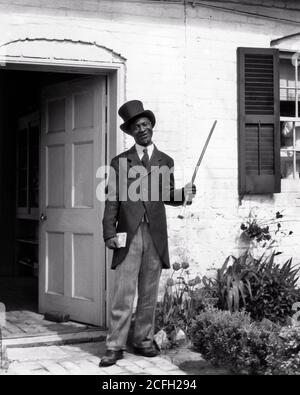 IN DEN 1930ER-JAHREN GASTFREUNDLICHER AFROAMERIKANISCHER BUSMANN, HISTORISCHES GEBÄUDE, IN DEM MAN BEGRÜSST WIRD HUT SCHWÄNZE BLICK AUF KAMERA FREDERICKSBURG VA USA - N1217 HAR001 HARS VOLLZEITPERSONEN VEREINIGTE STAATEN VON AMERIKA MÄNNER ÄLTER MANN ÄLTERER ERWACHSENER B&W NORDAMERIKA AUGENKONTAKT NORDAMERIKA SKILL BERUF FÄHIGKEITEN AFRO-AMERIKANER AFROAMERIKANER UND SCHWÄNZE SCHWARZEN ETHNIZITÄT STOLZ IN AUTORITÄT BERUFE EINLADENDE KONZEPTIONELLE FÜHRER STILVOLLE MORGENMANTEL FREDERICKSBURG GREETER TOP HAT VA SCHWARZ UND WEISS HAR001 ALTMODISCH AFROAMERIKANER Stockfoto