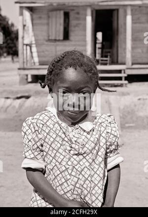 1930ER JAHRE SCHÜCHTERN LÄCHELND AFROAMERIKANISCHE KLEINE MÄDCHEN BLICK AUF KAMERA STEHEN VOR DER RAUEN LÄNDLICHEN HÜTTE HAUS SOUTH CAROLINA USA - N1736 HAR001 HARS HOME LIFE VEREINIGTE STAATEN KOPIERRAUM HALF-LENGTH INSPIRATION VEREINIGTE STAATEN VON AMERIKA KABINE RAUH B&W NORD AMERIKA BLICKKONTAKT NORDAMERIKA GLÜCK WELLNESS FRÖHLICH AFROAMERIKANER AFROAMERIKANER AFROAMERIKANER BLACK ETHNICITY STOLZ IN DER LÄCHELT KONZEPTUELL FRÖHLICH SCHÜCHTERN STILVOLL BENACHTEILIGTE WACHSTUM JUGENDLICHE SC SOUTH CAROLINA SCHWARZ-WEISS-ÄRA HAR001 ALTMODISCHE AFROAMERIKANER Stockfoto