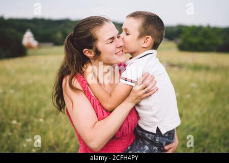 Frau verbringt Zeit mit einem Kind in der Natur. Mutter und Sohn umarmen im Park. Glückliche Mutter spielt mit ihrem Jungen auf dem Feld auf einer Lichtung. Spaß haben Stockfoto