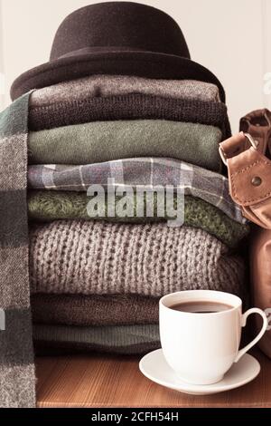 Haufen von grünen und grauen Pullover mit einem schwarzen Hut auf der Oberseite und einem heißen Getränk weißen Tasse auf der Seite, Hintergrund mit Kopierraum, gemütlich, Hygge oder saisonalen Krieg Stockfoto