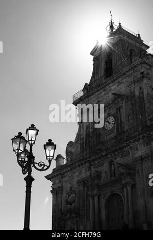 Barockkirche San Sebastiano di Palazzolo Acreide in schwarz Und weiß mit Sonnenstrahlen an der Spitze und einem Laternenpfosten Unten links Stockfoto