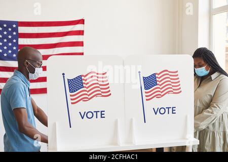 Seitenansicht Porträt von zwei afroamerikanischen Menschen in Masken, die am Tag nach der Pandemie in Wahlkabinen gegenüber stehen, Kopierraum Stockfoto