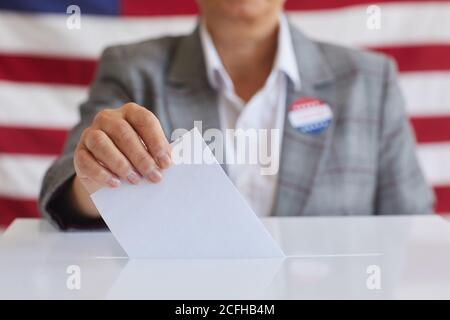 Nahaufnahme einer reifen Frau, die am Wahltag gegen die amerikanische Flagge steht und Stimmzettel in die Wahlurne legt, Platz kopieren Stockfoto