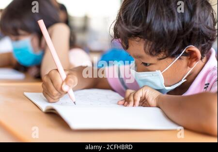 Schuljunge trägt Maske und Studie im Klassenzimmer Stockfoto