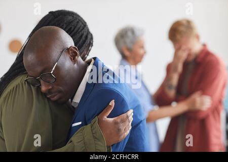 Seitenansicht auf zwei afroamerikanische Leute, die sich während des Unterstützunggruppentreffens umarmen, einander mit Druck, Angst und Trauer helfen, Raum kopieren Stockfoto