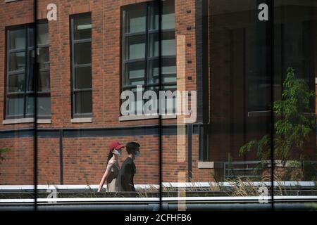 New York City, USA. September 2020. In den nahe gelegenen Fenstern spiegeln sich zwei Personen mit Masken, die am 5. September 2020 im High Line Park im neu eröffneten Bereich in New York, NY, spazieren. Der High Line Park erweiterte den Parkzugang zur 30th Street, nachdem er vor kurzem für Besucher mit mehreren Einschränkungen wieder geöffnet wurde, einschließlich der Anmeldung für ein Zeitfenster mit einem Abstand von 15 Minuten, Einfahrt nur durch die Gansevoort Street, nur auf einem Einbahnweg mit sozialen Distanzmarkierungen und Ausfahrt an der 23rd Street. (Anthony Behar/Sipa USA) Quelle: SIPA USA/Alamy Live News Stockfoto
