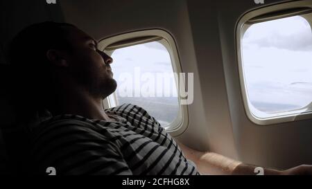 Junger Mann, der in das Fenster des Flugzeugs schaut, wenn es abhebt. Stockfoto