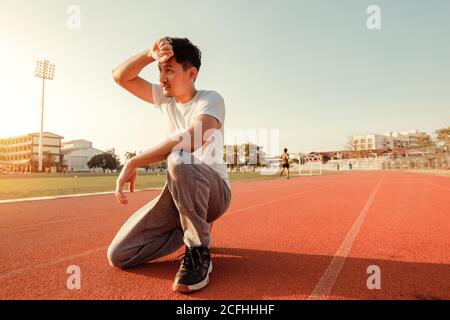 Müde nassen athletischen Mann wischen Schweiß seine Hand im Sportstadion mit Sonnenuntergang. Stockfoto