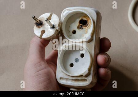 Ein Elektriker demonstriert eine verbrannte Steckdose. Weißes Verlängerungskabel nach Kurzschluss in der männlichen Hand. Elektrische Sicherheit. Stockfoto