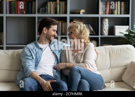 Glückliche reife Frau und junger Mann im Gespräch, auf der Couch sitzen Stockfoto