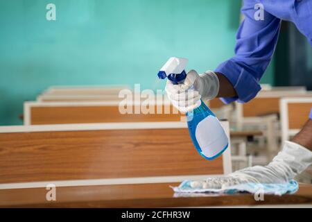 Nahaufnahme der Hände mit Handschuhen Desinfizieren Schreibtisch mit Desinfektionsmittel im Klassenzimmer - Reinigung von Staub auf der Tischoberfläche mit Tuch und Desinfektionsmittel auf sprühen Stockfoto