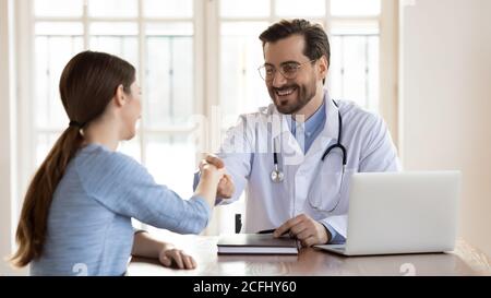 Lächelnder junger Arzt in Uniform, der die Hand der Patientin schüttelt Stockfoto