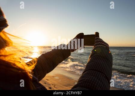 Frau Reisende fotografiert das Meer bei Sonnenaufgang auf einer Smartphone-Kamera. Stockfoto