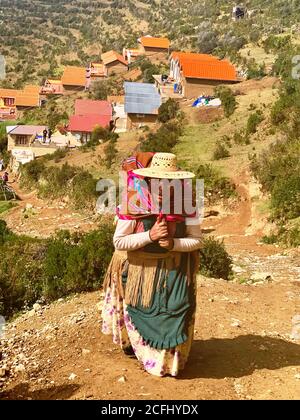 Alte signora von Isla del Sol, Bolivien. Bolivianische Aymara Frau in traditioneller Kleidung mit Aguayo klettert auf Hügel. Cholita indigene Frau aus Bolivien Stockfoto