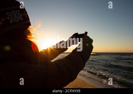 Frau Reisende fotografiert das Meer bei Sonnenaufgang auf einer Smartphone-Kamera. Stockfoto